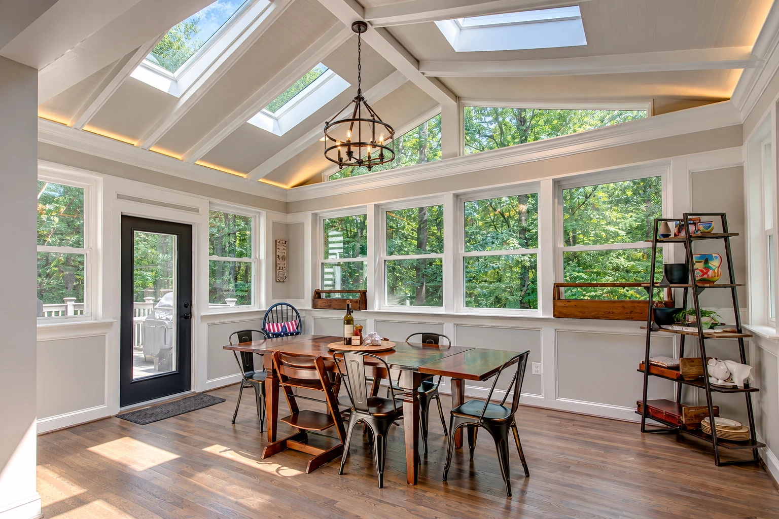 A bright four-season sunroom with a vaulted skylight ceiling, large windows and a dining table surrounded by chairs.