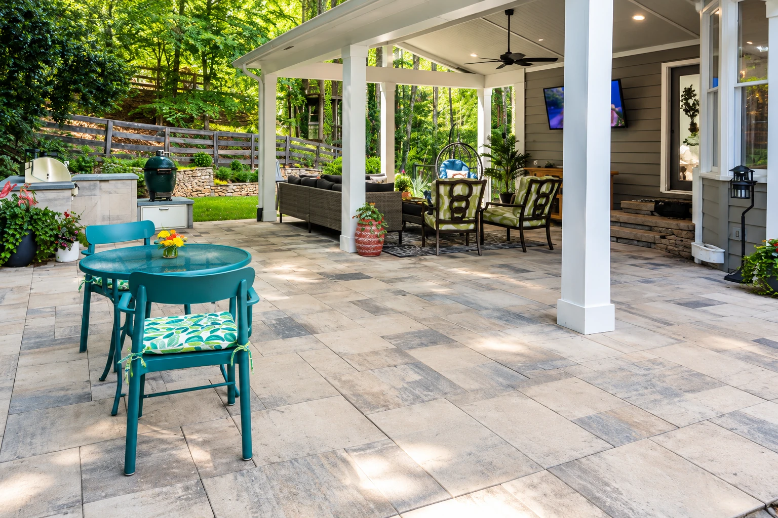 A covered patio with white columns shelters dining furniture beside a stone-tiled outdoor area and garden.