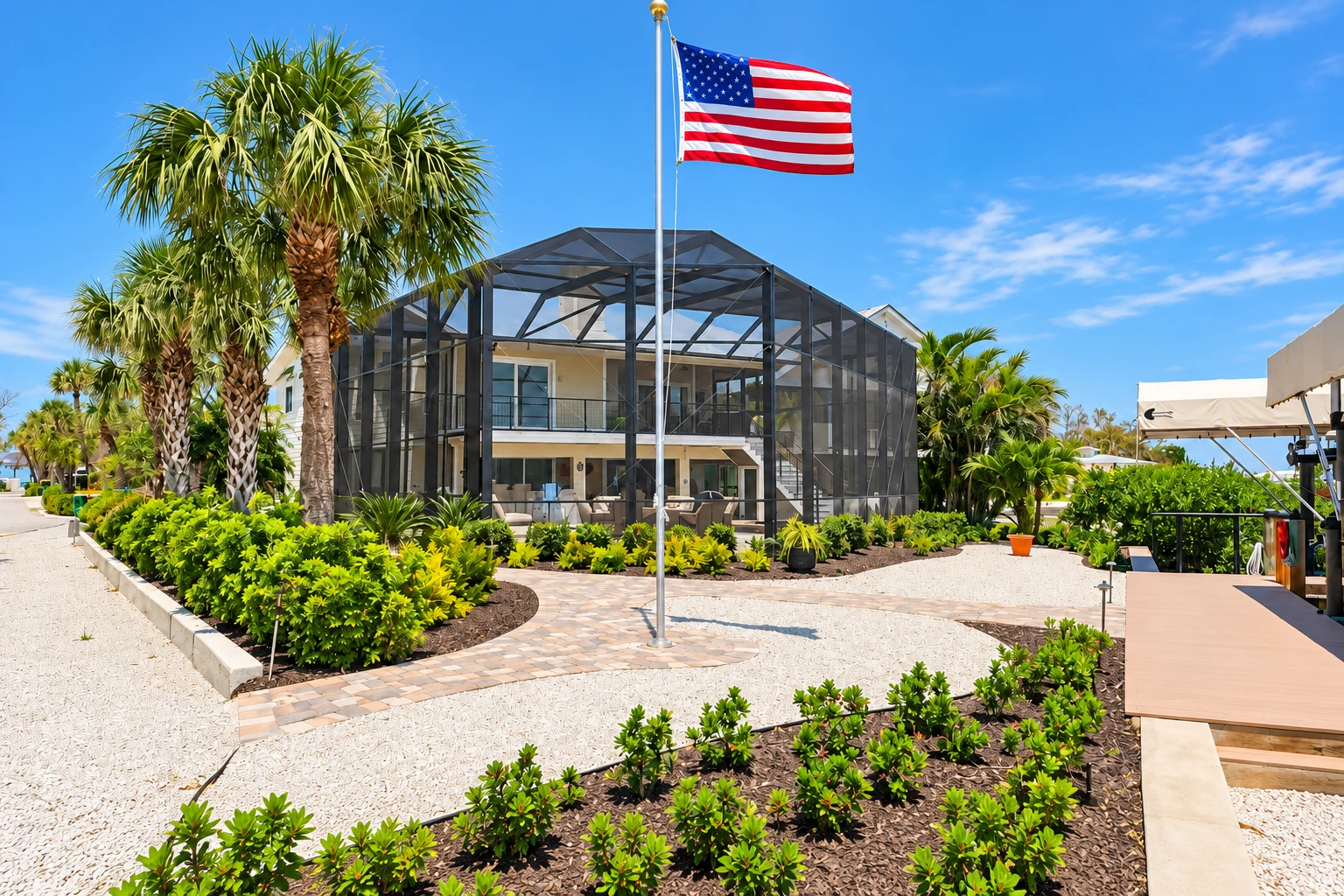 A large screened patio enclosure surrounds a two-story house, with palms, landscaped gravel beds and a flagpole in front.