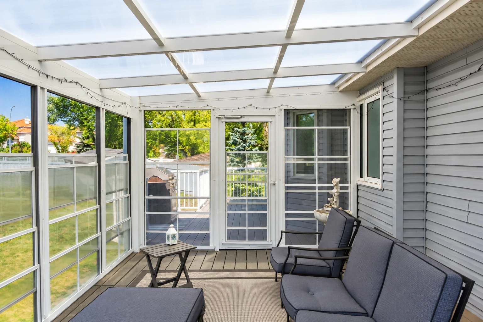 A screened three-season room with a translucent roof, wide windows and gray outdoor seating.