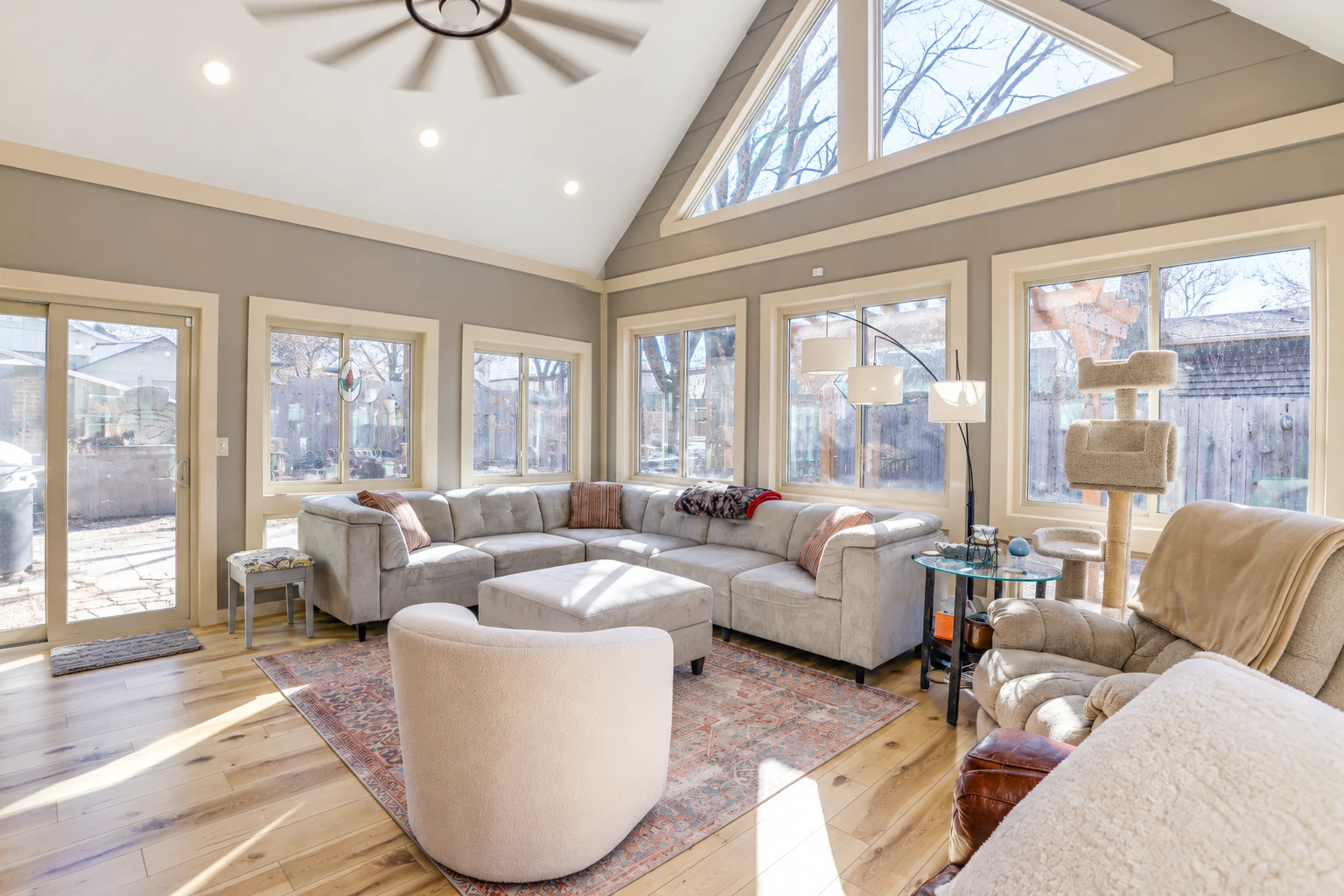 Sunroom living area with a vaulted ceiling, large windows, a sectional sofa, and a view of a fenced yard.